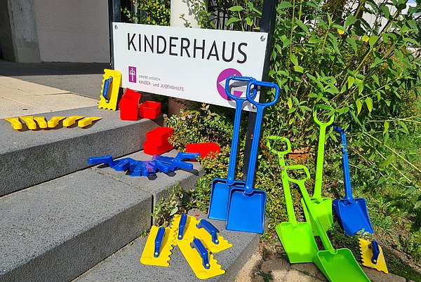 Buntes Kinderspielzeug vor einem Schild mit Aufschrift 'Kinderhaus' – das Bild verlinkt auf die Seite des Kinderhauses